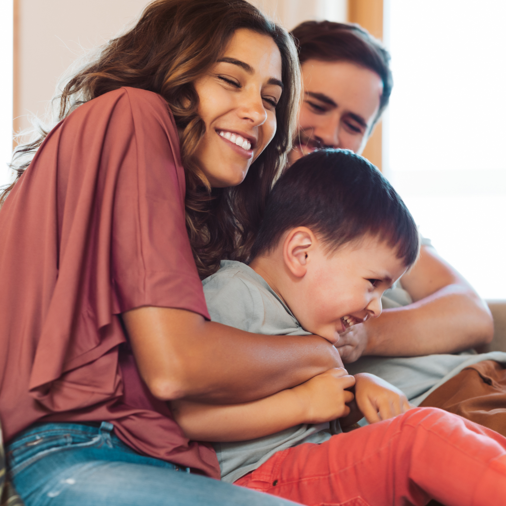 A mother, father, and son smiling and playing on a couch together