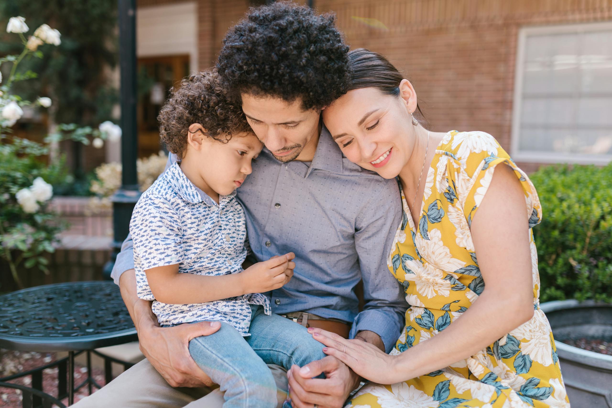 A happy family sitting on a bench, sharing affection and smiles in a garden setting.